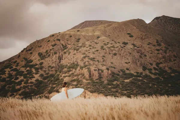 Surfer in golden wheat field with mountain